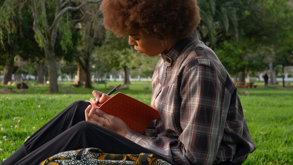 Black woman with afro sitting outside with journal